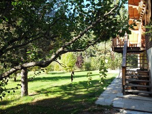 A wooden cabin with a balcony, surrounded by a grassy yard and trees. - Homerez - Chalet in Saint-Chaffrey, mountain view (Saint-Chaffrey)