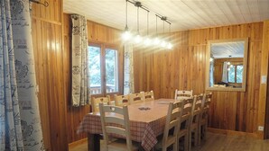 A dining area with a wooden table and chairs, a window with curtains, and a mirror on the wall. - Homerez - Chalet in Saint-Chaffrey, mountain view (Saint-Chaffrey)