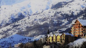 A snow-covered mountain landscape with a row of multi-story buildings with balconies, likely a hotel or resort. - Homerez - Chalet in Saint-Chaffrey, mountain view (Saint-Chaffrey)
