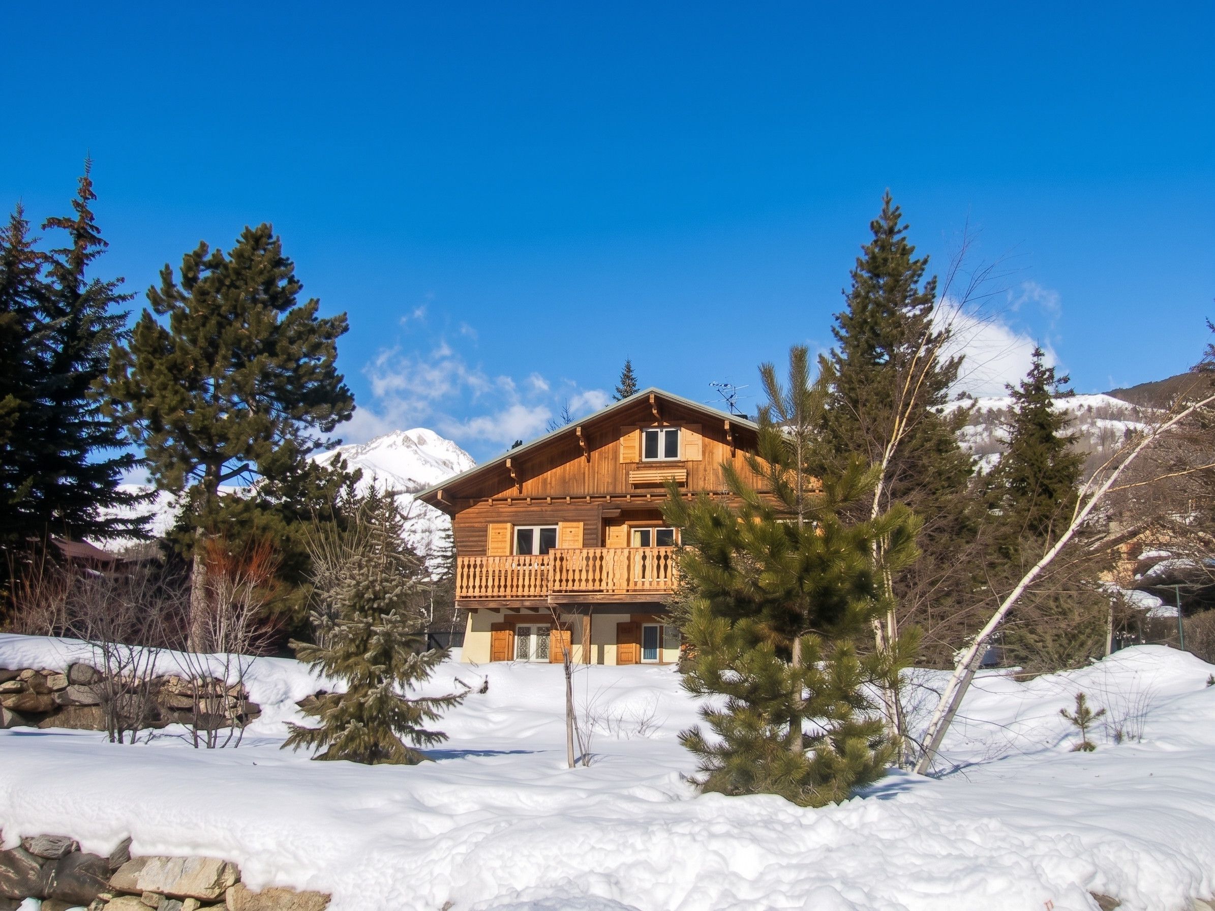 Un chalet en bois doté d’un balcon, entouré de neige et d’arbres, avec une montagne en arrière-plan.