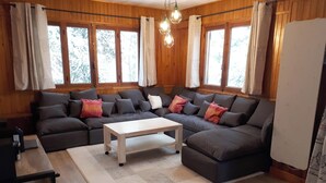 A cozy living room with a sectional sofa, a coffee table, and large windows with curtains. - Homerez - Chalet in Saint-Chaffrey, mountain view (Saint-Chaffrey)