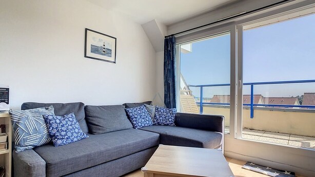 A modern living room with a grey sectional sofa, a wooden coffee table, and a large window offering a view of the cityscape. - 2-bedroom apartment near sea and center, includes parking (Cucq-Stella Plage)