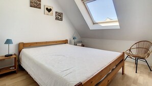 A bedroom with a sloped ceiling, a skylight, a wooden bed, a wicker chair, and wall art. - 2-bedroom apartment near sea and center, includes parking (Cucq-Stella Plage)