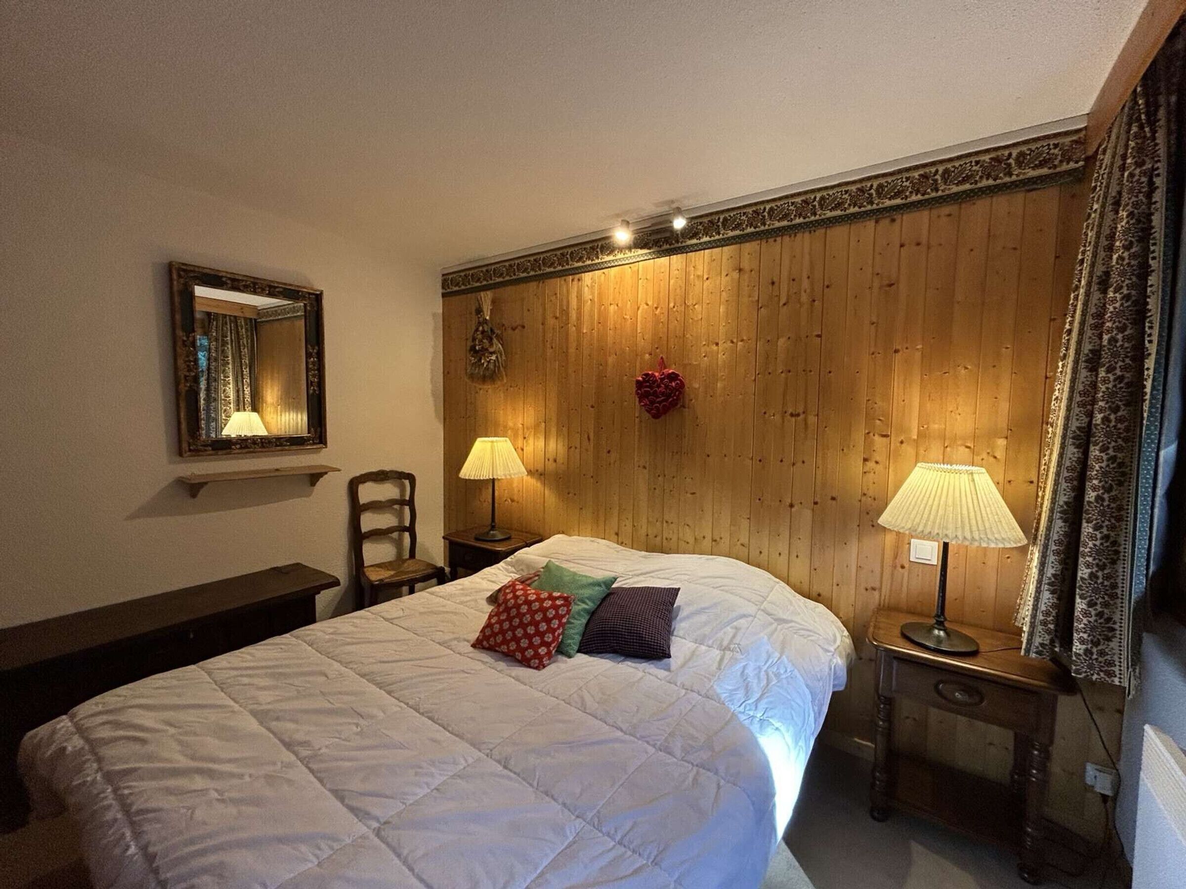 A bedroom with a wooden headboard, two bedside lamps, a mirror, and a bed with a quilt and pillows.