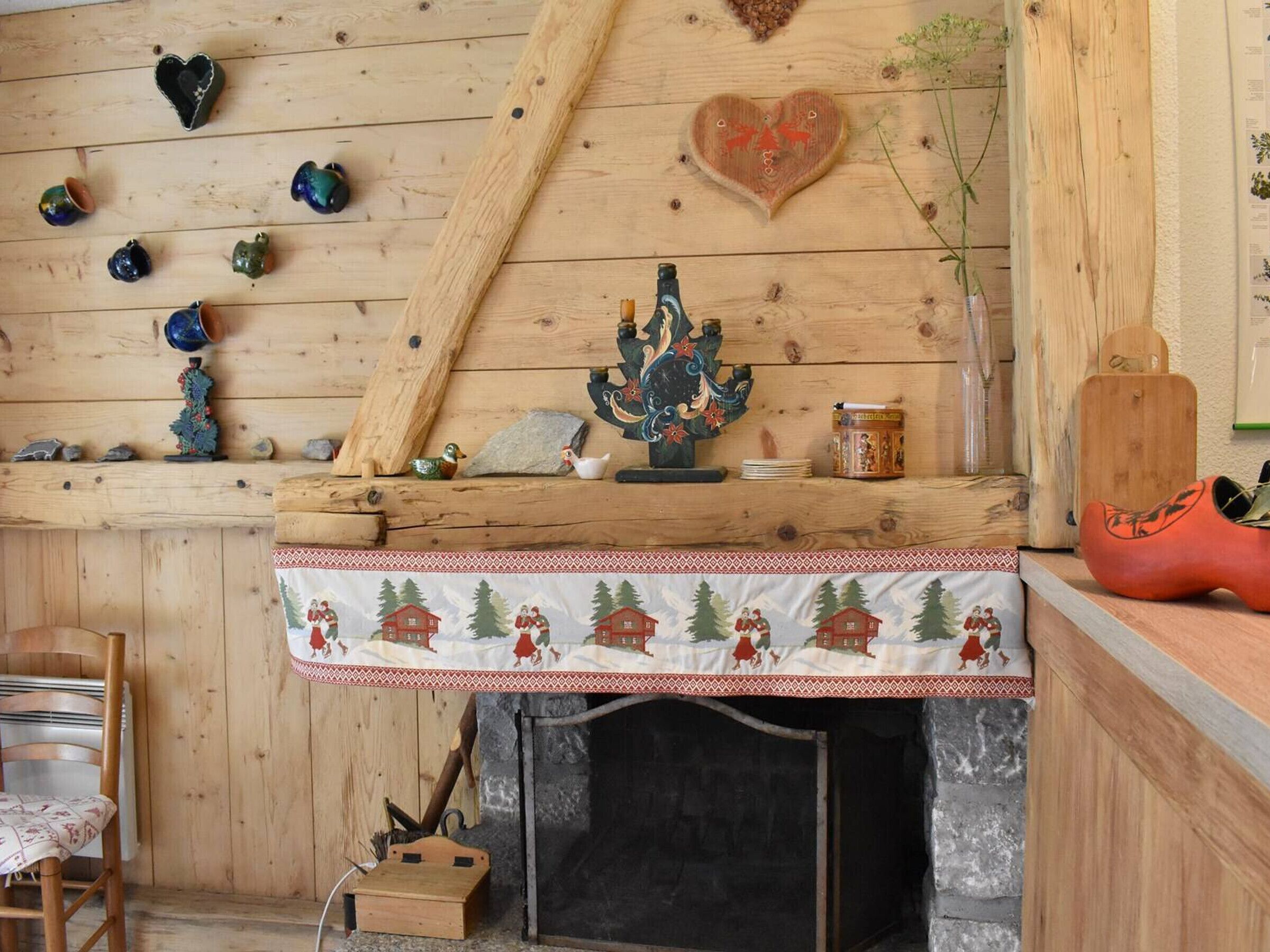 A rustic room with a wooden wall, a fireplace, and various decorative items including a heart-shaped ornament and a Christmas-themed tablecloth.