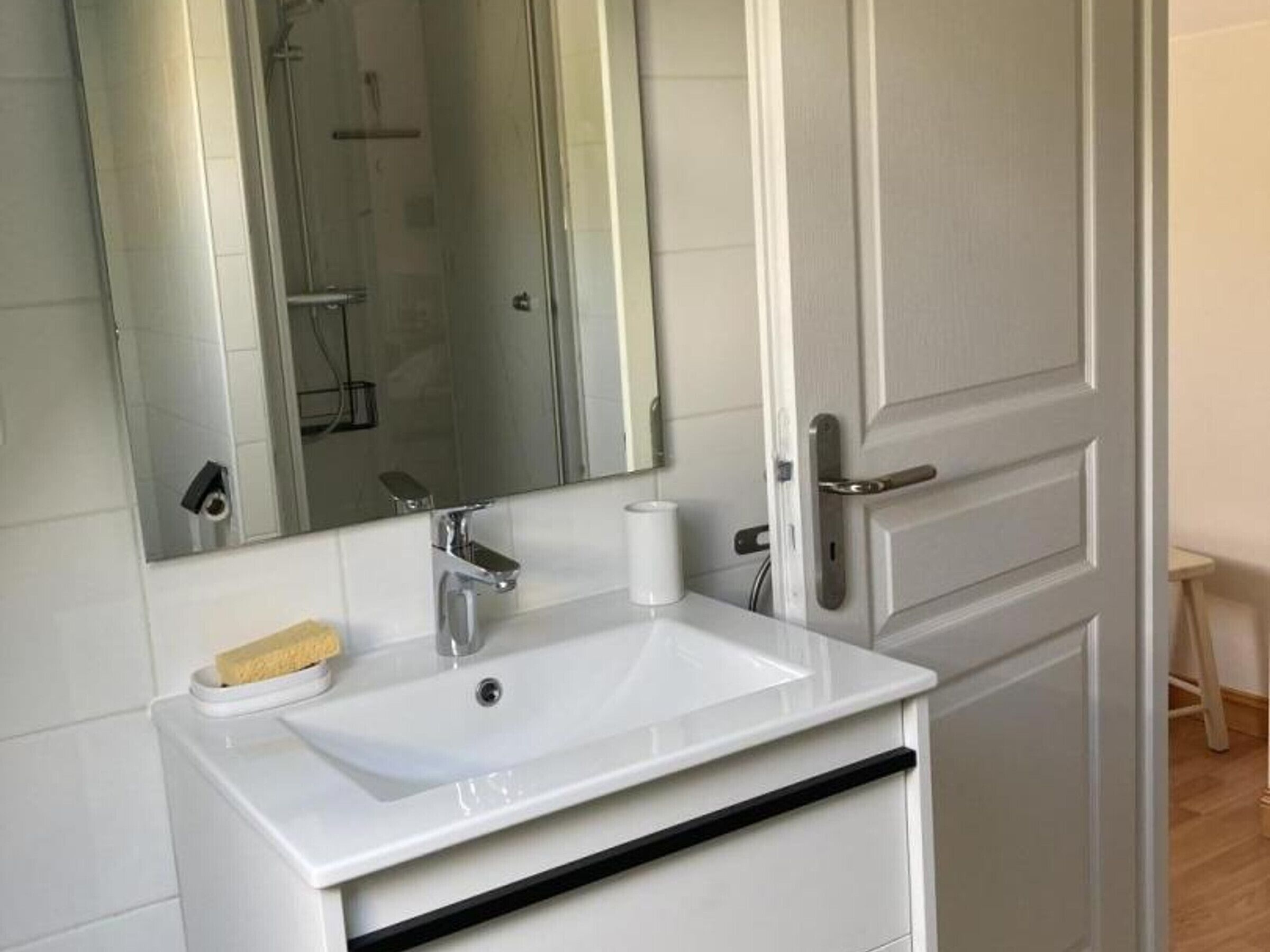 A bathroom with a white sink, a mirror, and a shower visible in the background.
