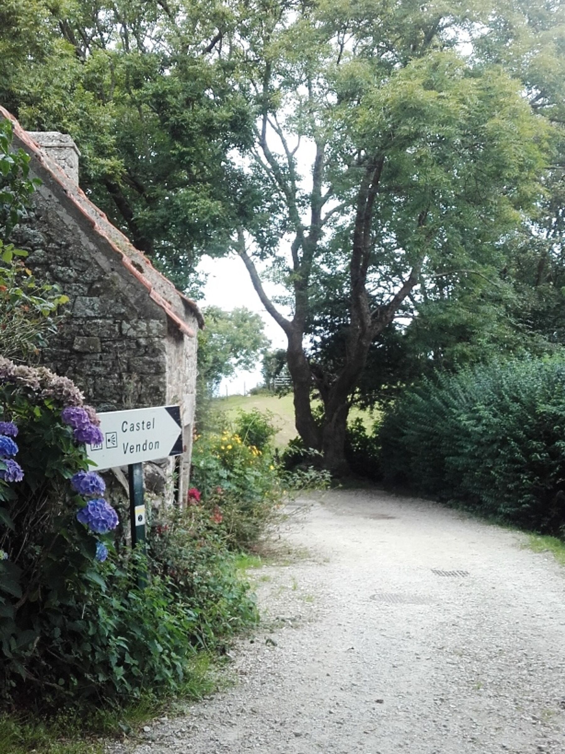A rural path leading to a stone building with a sign indicating directions to Castel and Vendon.