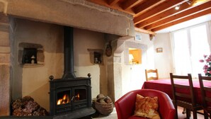 A cozy room with a stone fireplace, wooden beams, a red chair, and a dining table with chairs.
