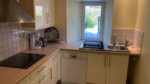 A compact kitchen with a stove, dishwasher, and a window with a view of greenery.