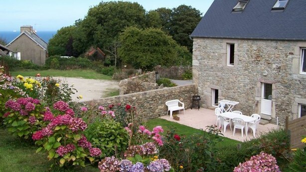 A stone house with a garden, outdoor seating, and a view of the sea.