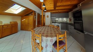 Une cuisine avec des meubles de rangement en bois, une table à manger avec des chaises et une lucarne au-dessus de la table.