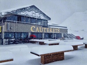 A building named "CAUTERETS" with a snow-covered roof and benches in front.