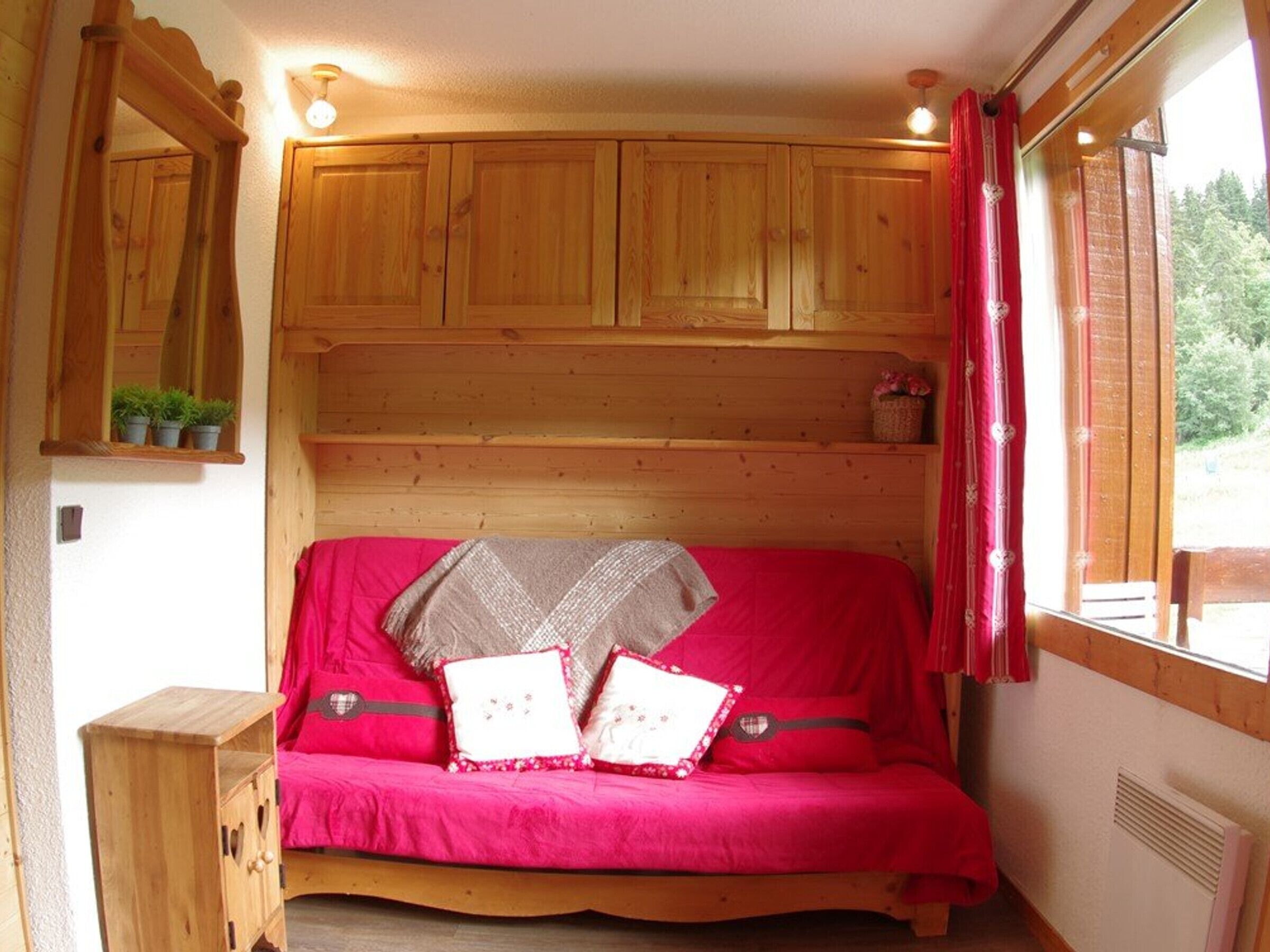 A cozy room with a wooden bed, a small wooden cabinet, and a window with curtains.