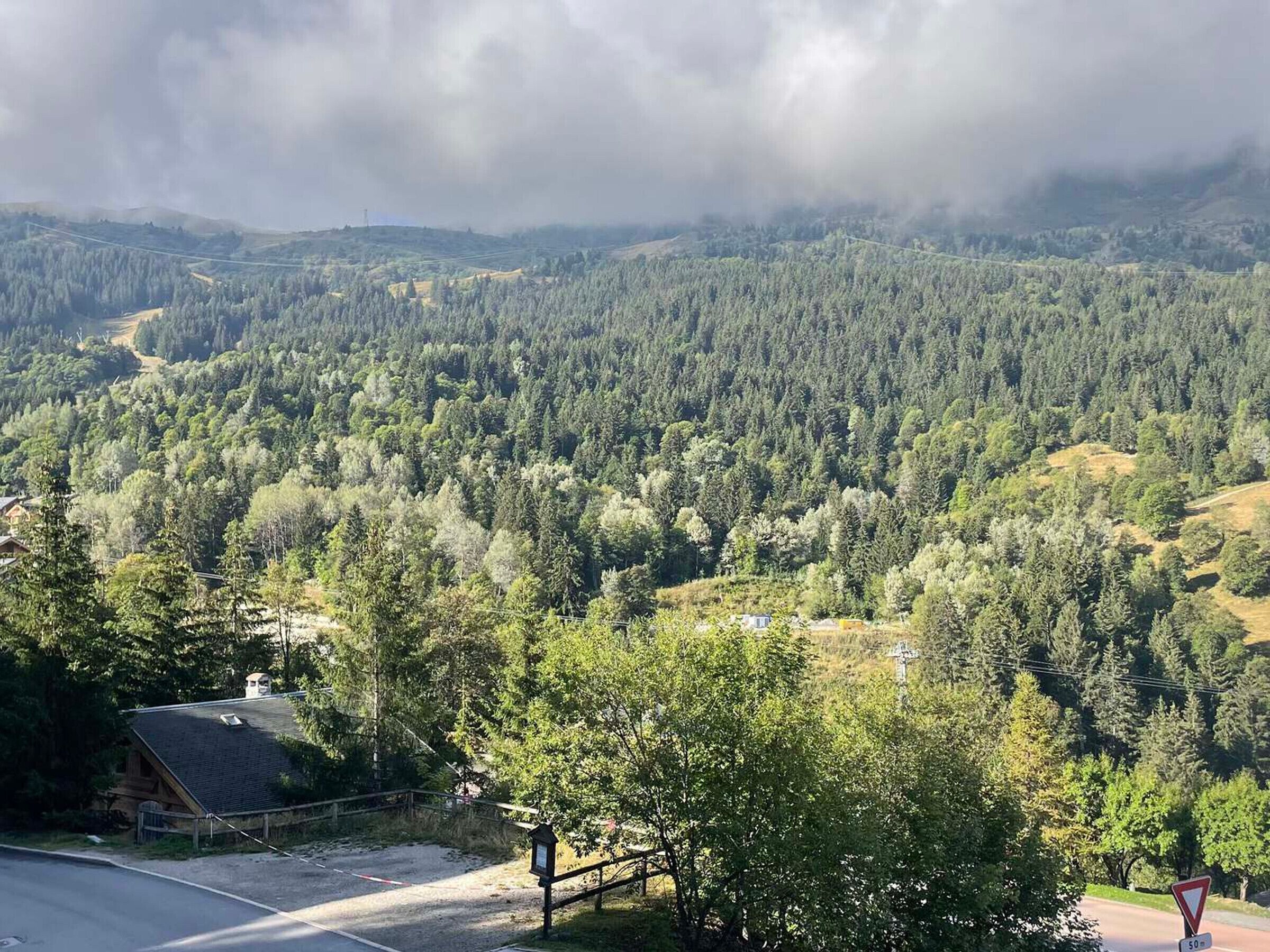 A mountainous landscape with dense forests, a small building, and a road.