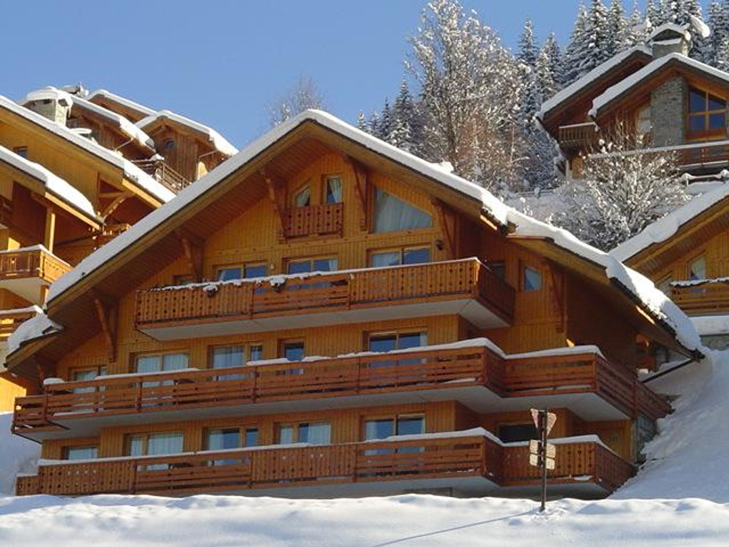 A multi-story wooden lodge with balconies, surrounded by snow-covered trees.