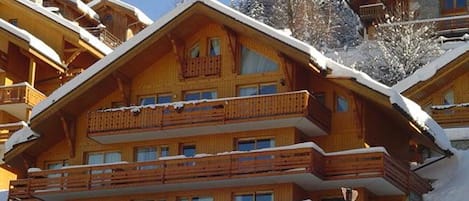 A multi-story wooden lodge with balconies, surrounded by snow-covered trees.