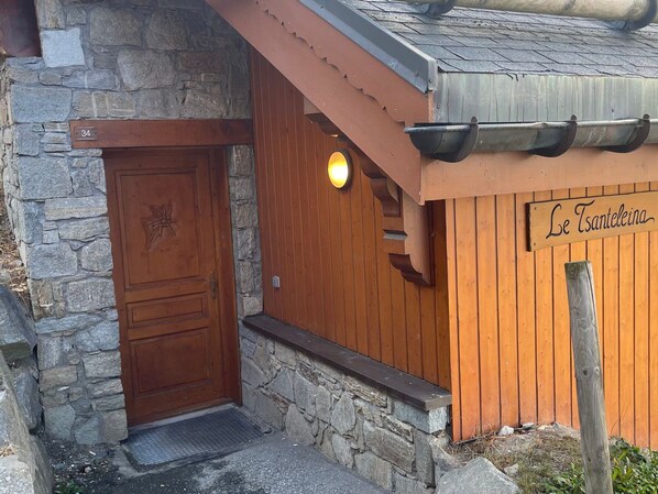 Une porte en bois, un mur en pierre, un porche en bois et une enseigne sur laquelle on peut lire « Le Tsanteleina ».