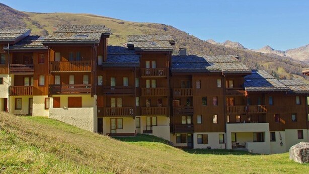 Une rangée de bâtiments en bois à plusieurs étages, dotés de balcons, se dressant sur un fond de montagnes.