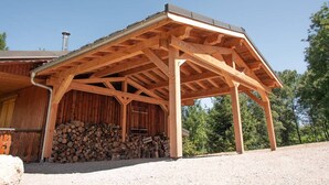 A wooden barn with a covered porch, a stack of firewood, and a gravel driveway. - Renovated 7-room chalet in Valmorel, 15 people, parking, terrace (Valmorel)