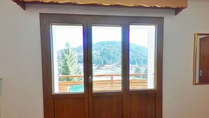 A room with a large wooden door leading to a balcony with a view of a mountainous landscape.