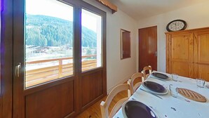 A dining area with a table set for four, large windows with a mountain view, wooden cabinets, and a wall-mounted clock.