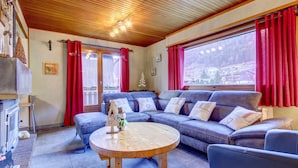 Una sala de estar acogedora con techo de madera, un sofá azul y una mesa de centro redonda de madera, además de una chimenea.