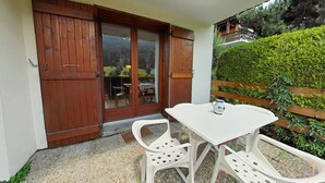 A patio with a white table and chairs, a wooden door, and a view of a garden. - Studio with Terrace and Ski Locker - Le Grand-Bornand (Le Grand-Bornand)