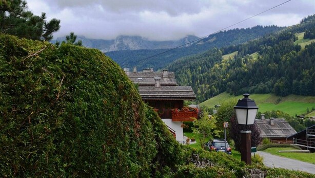 A traditional chalet with a sloped roof, surrounded by lush greenery and a mountainous backdrop. - Studio with Terrace and Ski Locker - Le Grand-Bornand (Le Grand-Bornand)