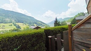 A wooden deck with a view of a mountainous landscape, including a house and a hedge. - Studio with Terrace and Ski Locker - Le Grand-Bornand (Le Grand-Bornand)