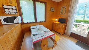 A wooden interior with a dining table set for four, a microwave, a television, and a window with curtains. - Studio with Terrace and Ski Locker - Le Grand-Bornand (Le Grand-Bornand)