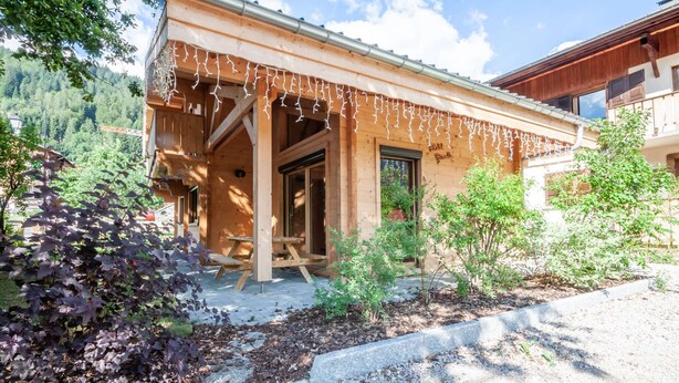 A wooden building with a covered entrance and a small garden area with plants and gravel. - Griotte: Beautiful chalet in the center of Morzine (MORZINE)