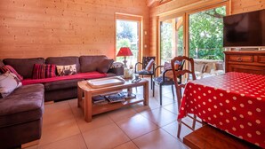 A cozy cabin-style room with a wooden interior, a sofa, a coffee table, a dining table with a polka dot tablecloth, and a television. - Griotte: Beautiful chalet in the center of Morzine (MORZINE)