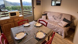 Un coin repas avec une table dressée pour deux personnes, un canapé orné de motifs papillon et une vue sur les montagnes par une grande fenêtre.