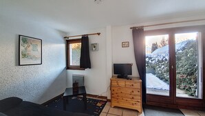 A room with a wooden dresser, a television, a framed picture on the wall, and a window with a view of snow-covered trees.