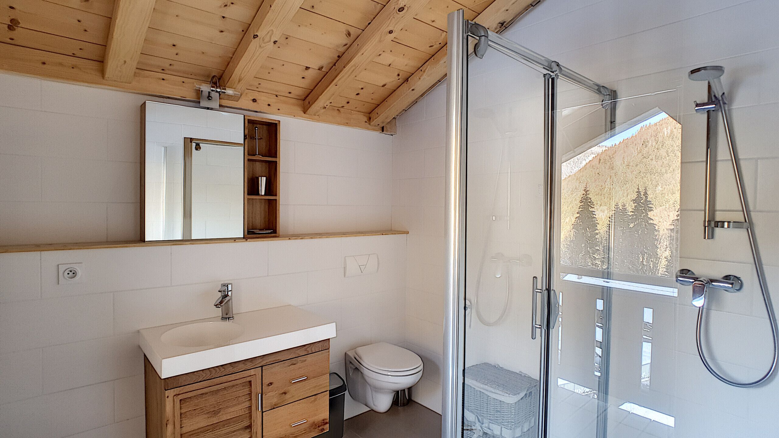 Une salle de bain avec un plafond en bois, une douche en verre, un lavabo blanc et des toilettes.