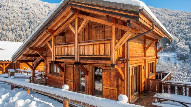Une cabane en bois dotée d’un balcon, entourée d’arbres et de montagnes couverts de neige.