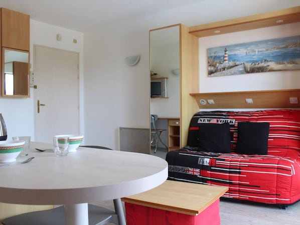 Una habitación con una mesa de comedor redonda, un sofá a rayas negras y rojas, un cuadro de un faro y un espejo en la pared.