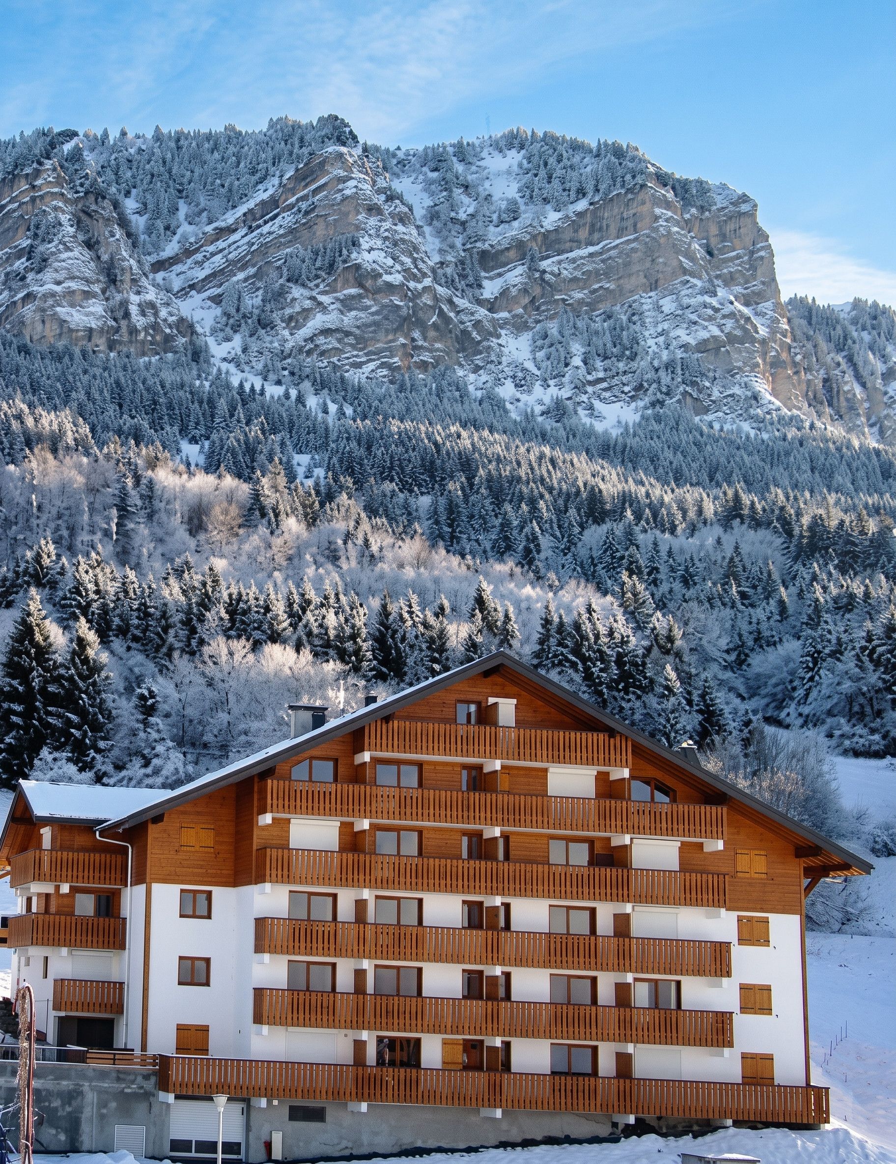 Ein mehrstöckiges Holzgebäude mit Balkonen vor einer verschneiten Berglandschaft.