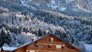 Ein mehrstöckiges Holzgebäude mit Balkonen vor einer verschneiten Berglandschaft.