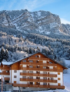 Un edificio de madera de varios pisos con balcones, con una imponente montaña nevada de fondo.