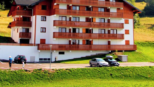 Un immeuble à plusieurs étages, doté de balcons, qui se dresse sur un fond de paysage montagneux.
