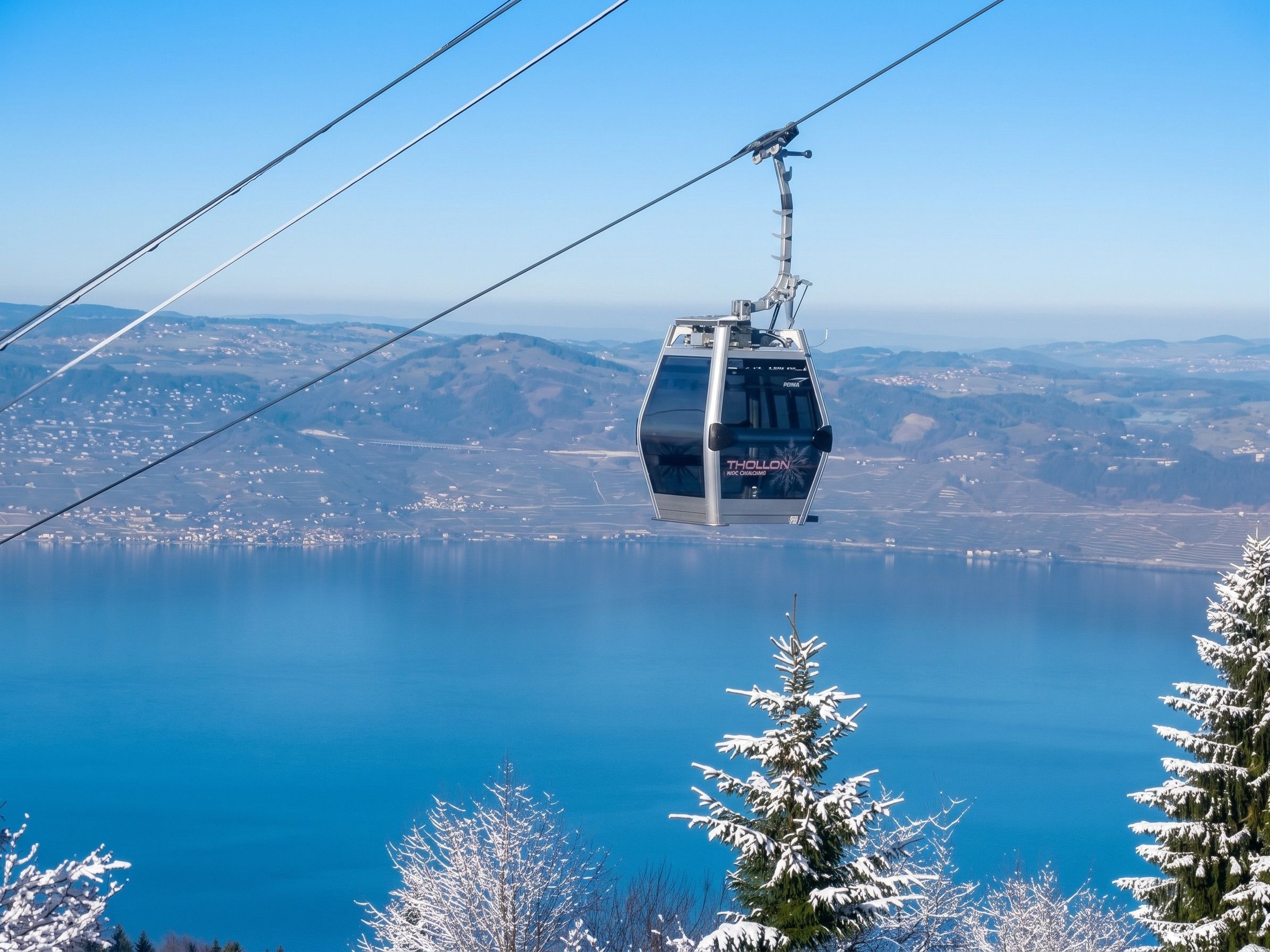 Un teleférico suspendido sobre una masa de agua con árboles nevados en primer plano.