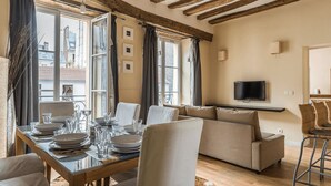 A dining area with a wooden table set for four, a sofa, and a TV mounted on the wall.