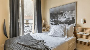 A hotel room with a bed, a view of a cityscape through a window, and a balcony with a railing.