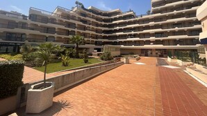 A multi-story hotel with a central courtyard, featuring a brick pathway and landscaped areas with palm trees. - Beachfront 2-Room Apartment with Terrace in Fréjus, Sleeps 4 (Fréjus)