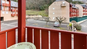 A balcony with a view of a parking lot, a building with red window frames, and a hill with trees in the background. - Studio cabin in Esquièze-Sère for 6 with balcony, mountain view and parking (Esquièze-Sère)