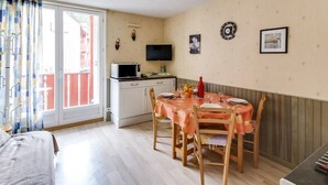 A compact room with a dining table set for four, a television, and a kitchenette. - Studio cabin in Esquièze-Sère for 6 with balcony, mountain view and parking (Esquièze-Sère)