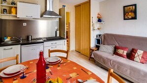 A compact kitchen with a stove, sink, and cabinets, a dining table set for two, and a sofa in the adjacent living area. - Studio cabin in Esquièze-Sère for 6 with balcony, mountain view and parking (Esquièze-Sère)