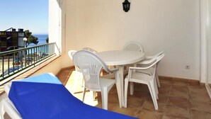 Un balcón con mesa y sillas, una sombrilla azul y vista al mar.