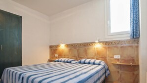 Un dormitorio con cama, mesita de noche, lámpara de pared y ventana con cortinas.